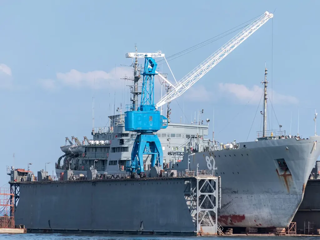 Naval vessel moored alongside a shipyard crane